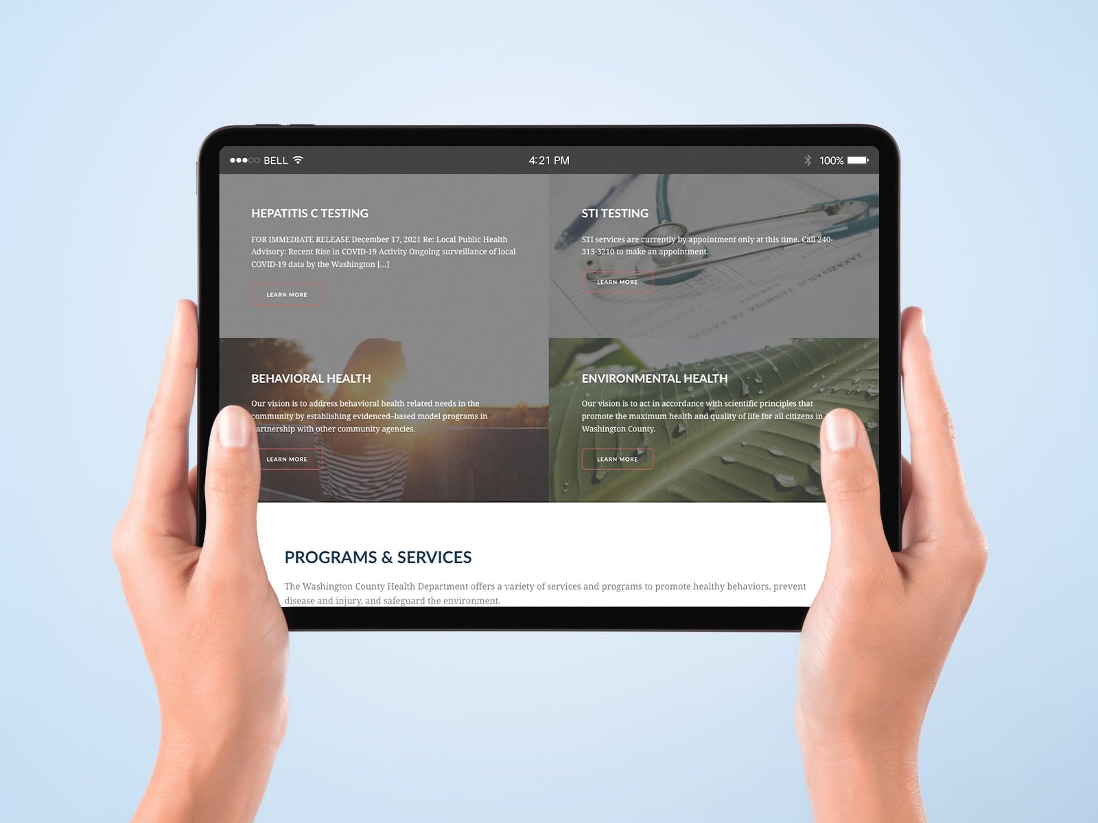 Hands holding a tablet displaying a health department website. The screen shows sections on hepatitis testing, STI testing, behavioral health, and environmental health, with descriptions and 