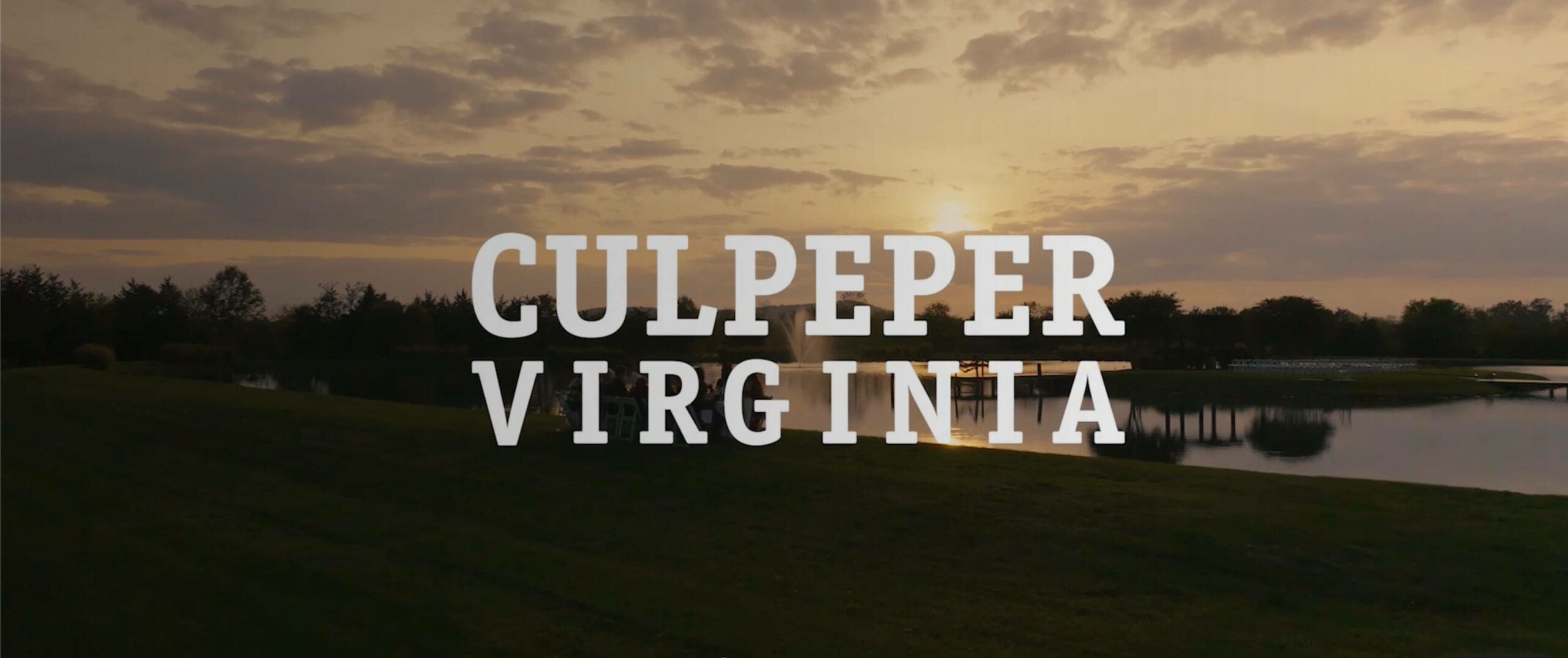 Sunset view over a grassy field and pond with trees in the background. Large white text in the center reads, 