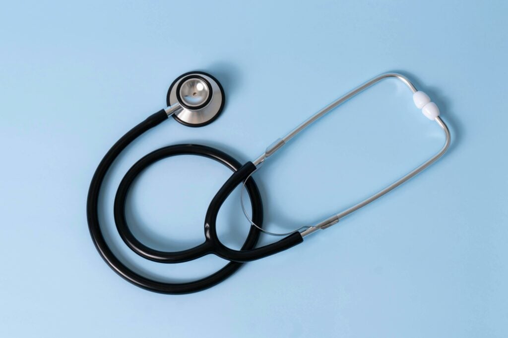 A black and silver stethoscope is placed on a light blue background, with the tubing curled in a loose coil.