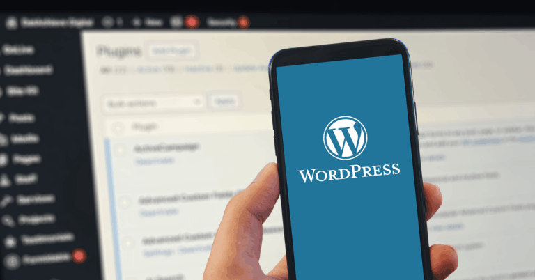 A person holds a smartphone displaying the WordPress logo and text, with a blurred computer screen showing the WordPress plugins page in the background.